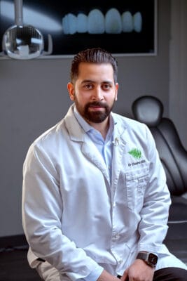 Portrait of Dr. Cheema sitting in a white lab coat in a dental treatment room.