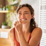 Woman brushing teeth with a wooden toothbrush in a bright bathroom, smiling during her oral hygiene routine